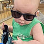 baby, child, sunglasses, green_shirt, shopping_cart, indoor, person, holding, footwear, cute, fashion, head, face, casual, shopping, toddler, skin, hand, seat, retail