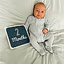 baby, infant, two_months, milestone_sign, onesie, striped_clothing, bed, sheet, lying_down, portrait, cute, smile, face, eyes, hand, feet, soft, neutral_colors, newborn, sleepwear