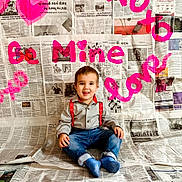Garrett is registered to the contest to win money with this photo: toddler, child, smiling, sitting, socks, jeans, shirt, suspenders, newspaper, background, floor, indoors, colorful, red, pink, blue, clothing, portrait, happy, casual