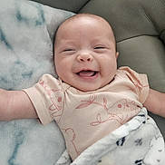 Sabrina is registered to the contest to win money with this photo: baby, smiling, blanket, couch, infant, happy, clothing, face, skin, comfort, cute, child, lying_down, cozy, soft, portrait, human, expression, indoors, relaxing