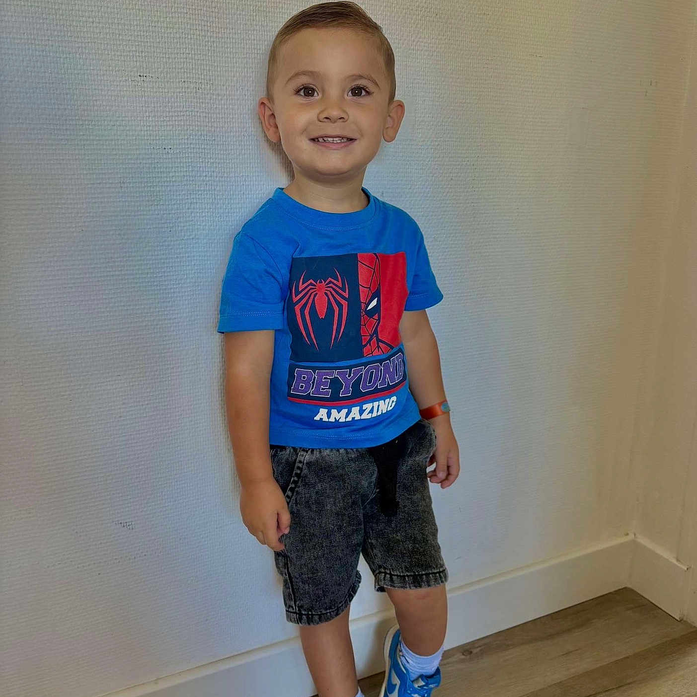 Kezyo a rejoint le concours — aidez-le/la à gagner de superbes lots ! blue_shoes, blue_tshirt, boy, casual_clothing, child, flooring, happy, indoor, person, portrait, short_hair, shorts, smiling, sneakers, spiderman, standing, wall, watch, white_socks, wooden_floor