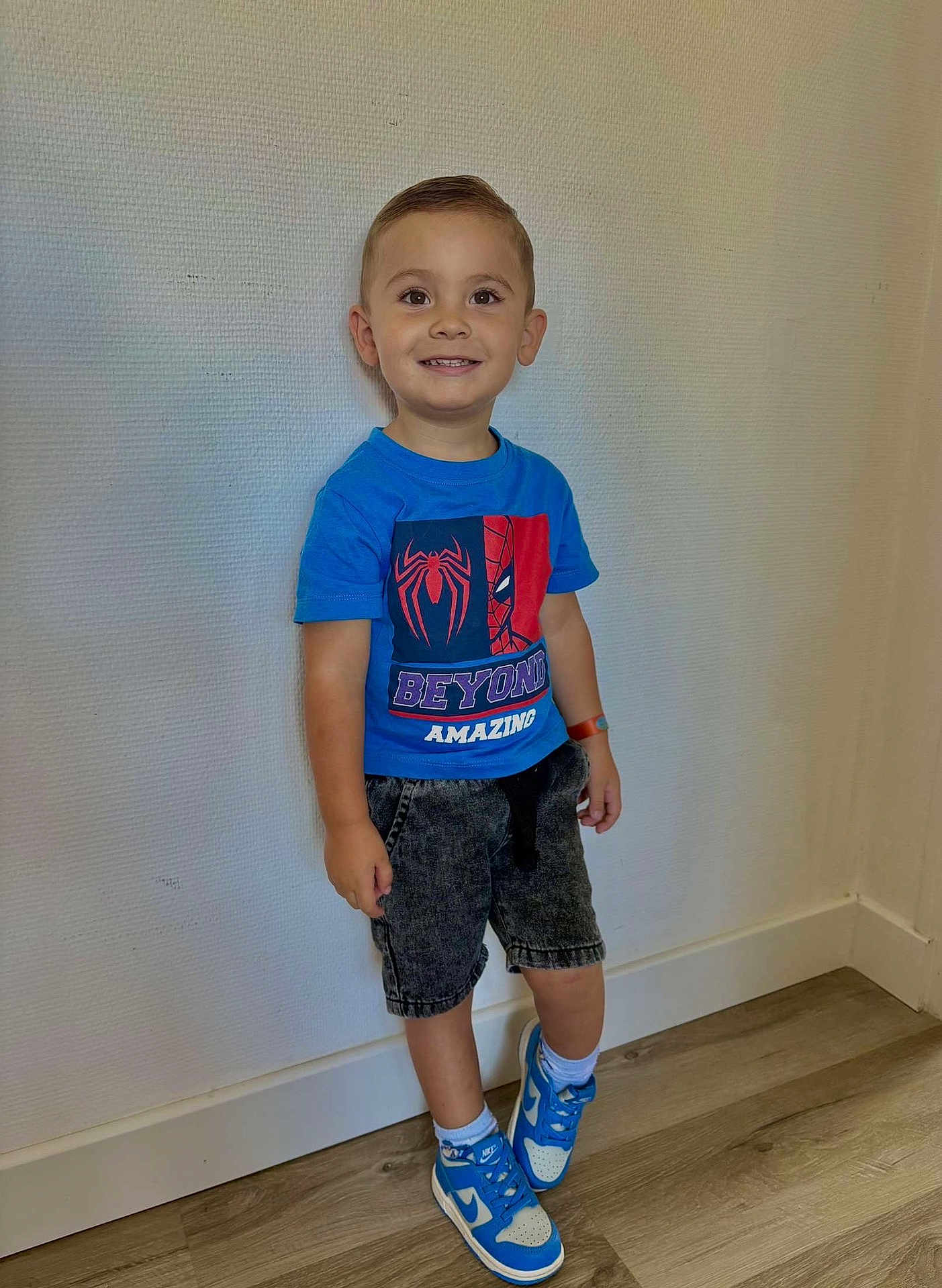 Kezyo a rejoint le concours — aidez-le/la à gagner de superbes lots ! child, boy, smiling, standing, blue_tshirt, spiderman, shorts, sneakers, blue_shoes, white_socks, wooden_floor, wall, indoor, casual_clothing, happy, portrait, person, short_hair, watch, flooring