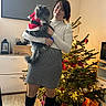 Twinkies participe au concours pour gagner de l'argent avec cette photo : woman, cat, christmas_tree, holiday, indoor, decorations, lights, presents, floor, boots, skirt, white_top, furniture, television, ornaments, gift_bag, wood_floor, smile, festive, costume