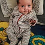 baby, infant, striped_clothing, pillow, blanket, smiling, hand, face, cute, lying_down, indoors, child, young, cozy, colorful, patterned, fabric, person, portrait, cute_expression