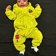 Brooklyn is registered to the contest to win money with this photo: baby, child, smile, green_onesie, grinch, socks, lying_down, black_background, infant, cute, happy, cozy_clothing, portrait, baby_clothes, childrens_wear, indoors, one_person, young_child, bright_color, soft_texture