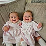 baby, twins, smiling, couch, indoor, cute, child, sitting, matching_clothes, pink_dress, white_socks, hair_bow, happy, infant, portrait, two_children, cozy, family, home, adorable