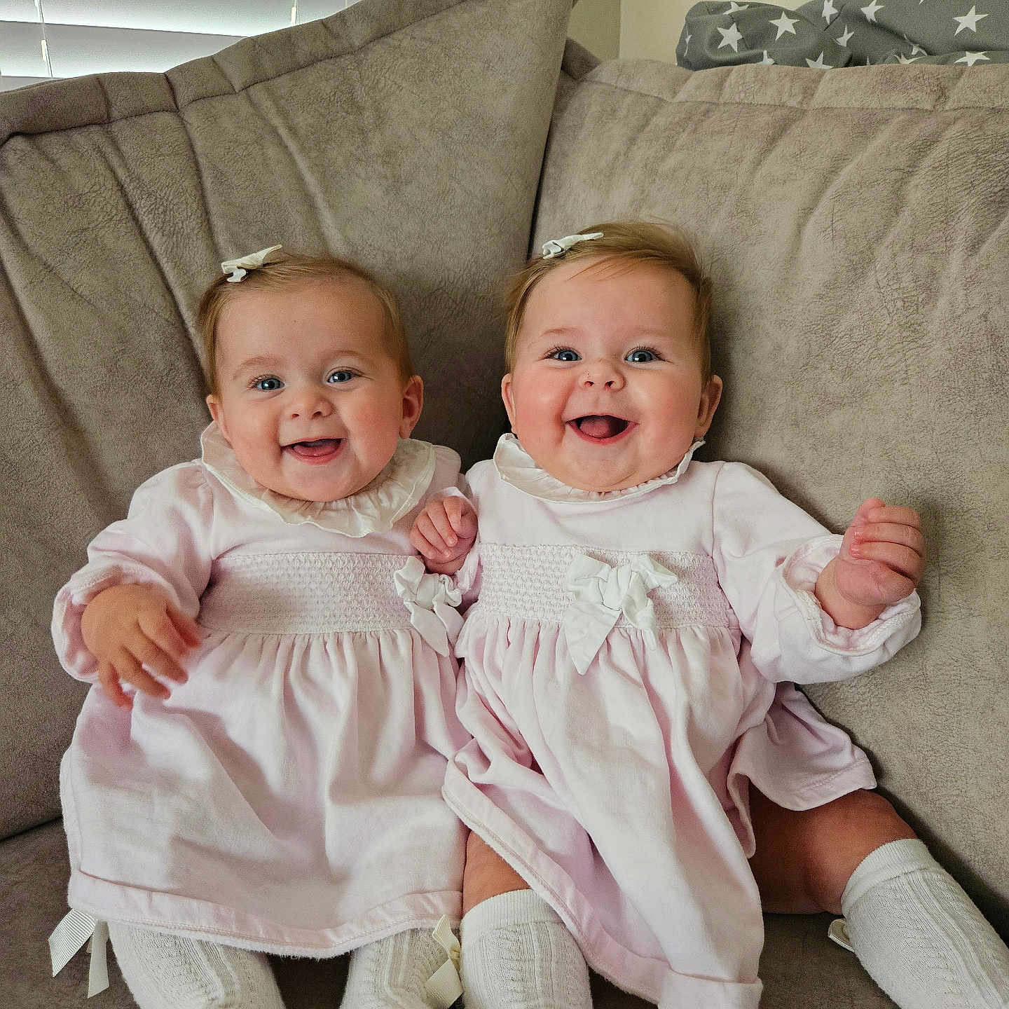Rosie And Gracie is registered to the contest to win money with this photo: adorable, baby, child, couch, cozy, cute, family, hair_bow, happy, home, indoor, infant, matching_clothes, pink_dress, portrait, sitting, smiling, twins, two_children, white_socks