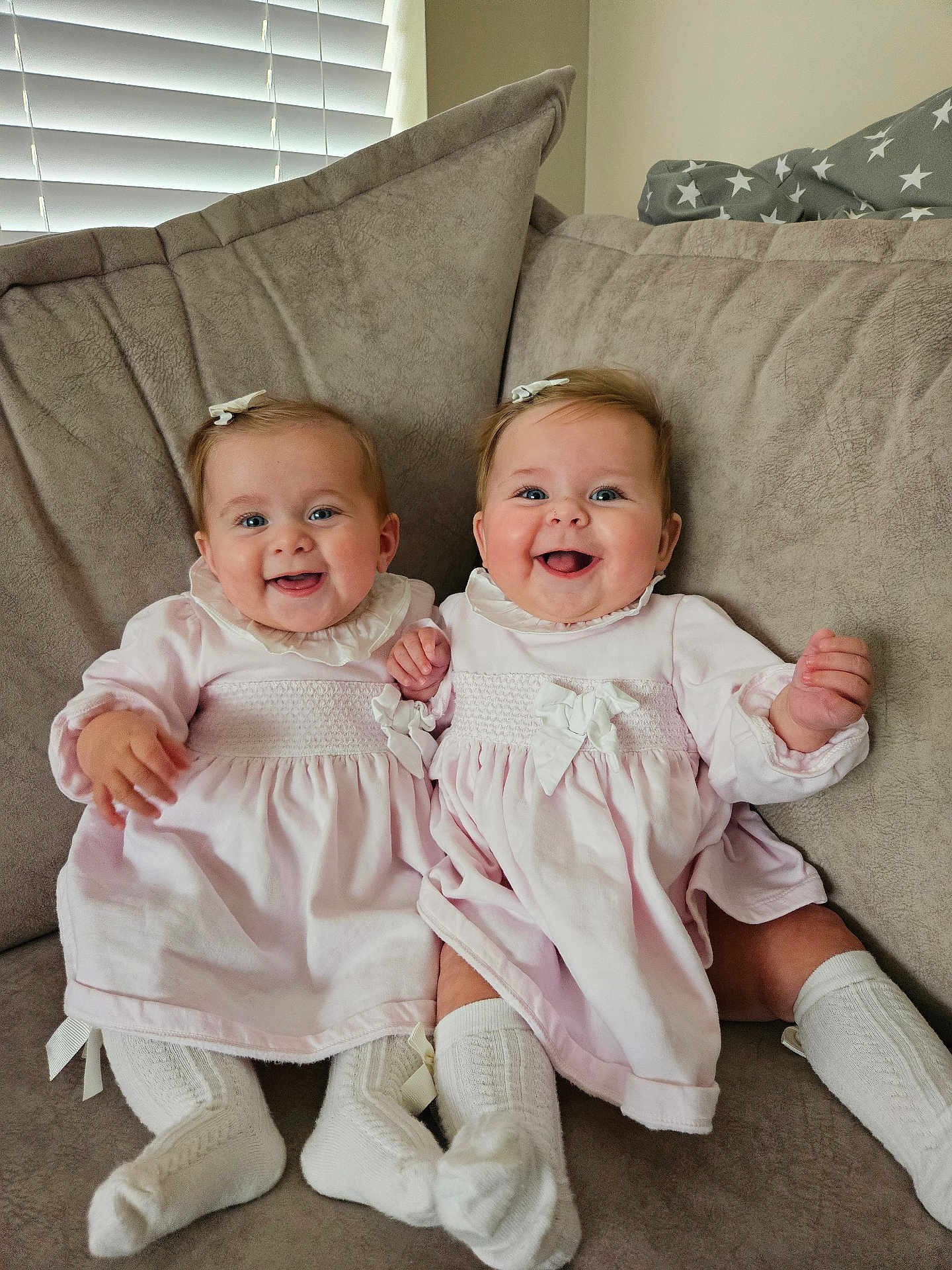 Rosie And Gracie is registered to the contest to win money with this photo: baby, twins, smiling, couch, indoor, cute, child, sitting, matching_clothes, pink_dress, white_socks, hair_bow, happy, infant, portrait, two_children, cozy, family, home, adorable