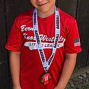 Nolan joined the competition — help win amazing prizes! american_flag_patch, baseball, boy, child, competition, dirt, grass, happy, medal, outdoor, pants, portrait, red_shirt, smile, sports, summer, team_uniform, trophy, wooden_fence, young_athlete