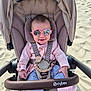 Romane participe au concours pour gagner de l'argent avec cette photo : baby, sunglasses, stroller, beach, sand, smile, child, person, clothing, jacket, pants, floral_pattern, footwear, pink, blue, outdoor, sunny, seatbelt, toy, accessory