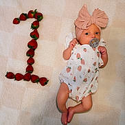 Scottie is registered to the contest to win money with this photo: baby, infant, strawberry, fruit, number_one, pacifier, headband, bow, clothing, cute, lying_down, blanket, pattern, skin, foot, hand, celebration, milestone, adorable, portrait