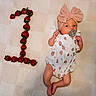 baby, infant, strawberry, fruit, number_one, pacifier, headband, bow, clothing, cute, lying_down, blanket, pattern, skin, foot, hand, celebration, milestone, adorable, portrait