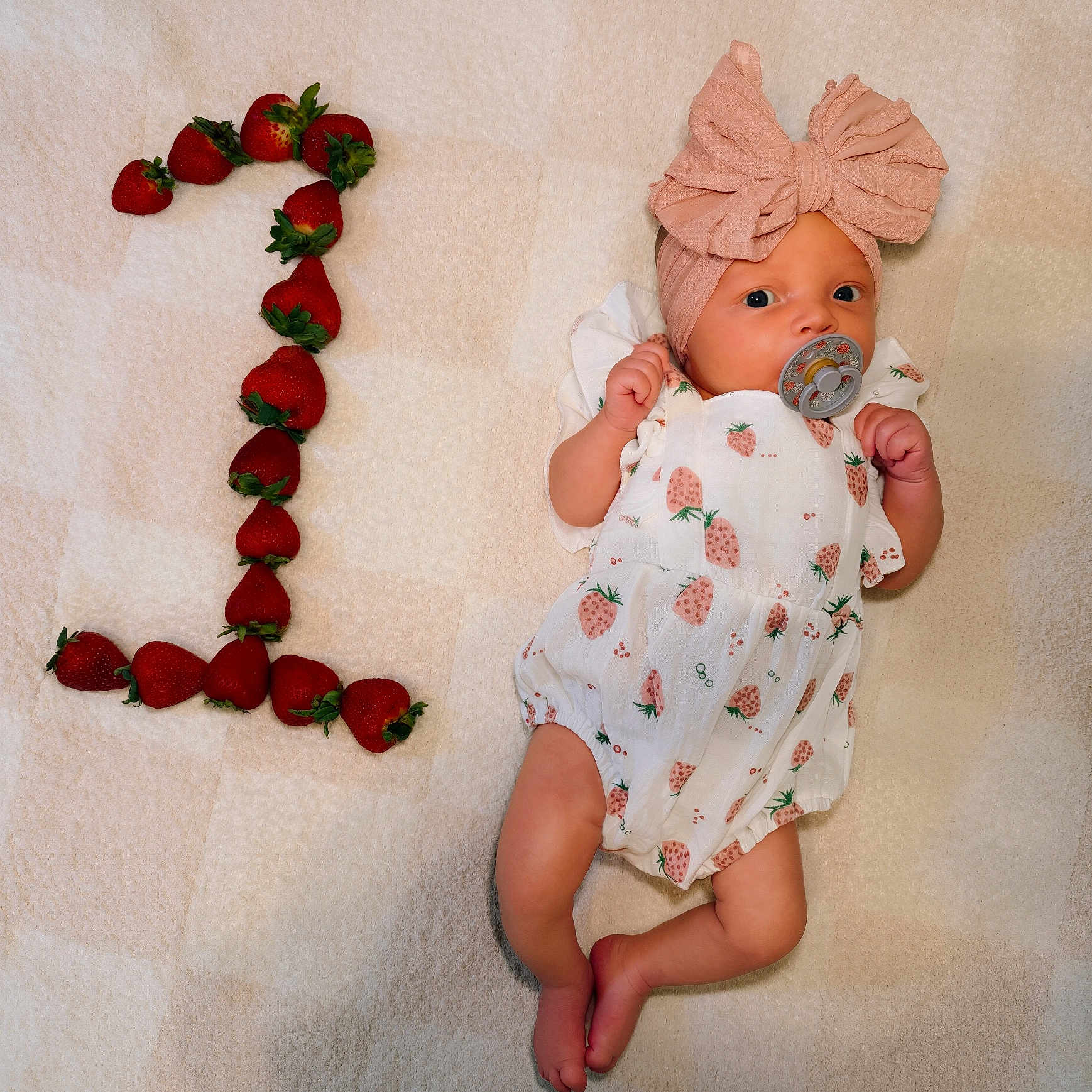 Scottie is registered to the contest to win money with this photo: baby, infant, strawberry, fruit, number_one, pacifier, headband, bow, clothing, cute, lying_down, blanket, pattern, skin, foot, hand, celebration, milestone, adorable, portrait