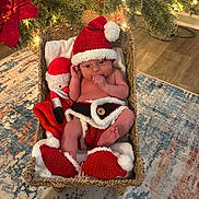 Bodie joined the competition — help win amazing prizes! baby, infant, christmas, holiday, basket, knit_hat, knit_booties, knit_diaper_cover, plush_toy, santa_hat, santa_outfit, indoors, floor_rug, decorations, lights, wood_floor, cute, festive, thumb_sucking, holiday_season