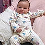 Alba a rejoint le concours — aidez-le/la à gagner de superbes lots ! baby, infant, smiling, pajamas, cartoon_print, cushion, pink, white, soft_texture, happy, face, child, cute, indoor, relaxed, seated, cozy, comfort, person, portrait