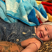Aurora is registered to the contest to win money with this photo: baby, smiling, denim_overalls, headband, blanket, colorful_blanket, tattooed_arm, infant, cute, cozy, indoor, portrait, happy, child, soft_texture, fabric, leisure, relaxed, person, clothing