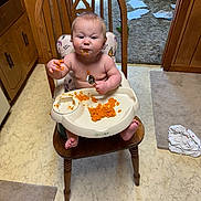 Sophie joined the competition — help win amazing prizes! baby, high_chair, messy, food, orange_food, wooden_chair, carpet, papers, whiteboard, kitchen, child, face, hand, floor, clothing, person, dining, tableware, spoon, indoor
