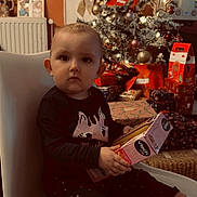 Alya participe au concours pour gagner de l'argent avec cette photo : child, toddler, baby, christmas_tree, presents, gift, toy, chair, sitting, indoor, portrait, festive, decoration, ornament, wrapping_paper, box, sock, radiator, holiday, face