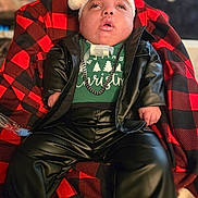 Jeremy is registered to the contest to win money with this photo: baby, chain_necklace, child, christmas_sweater, cozy, cute, face, fashion, festive, holiday, indoor, leather_jacket, leather_pants, medical_device, person, portrait, red_black_blanket, santa_hat, sitting, young_child