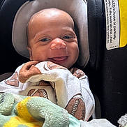 Damon is registered to the contest to win money with this photo: baby, smile, infant, car_seat, blanket, clothing, onesie, football_pattern, child, happy, face, seat, indoor, cute, headrest, closeup, baby_clothes, soft_texture, newborn, comfort