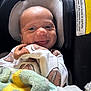 baby, smile, infant, car_seat, blanket, clothing, onesie, football_pattern, child, happy, face, seat, indoor, cute, headrest, closeup, baby_clothes, soft_texture, newborn, comfort