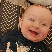 Jules a rejoint le concours — aidez-le/la à gagner de superbes lots ! baby, infant, smiling, happy, drooling, cute, face, eyes, cheeks, ear, hair, pillow, patterned_pillow, cushion, shirt, graphic_tshirt, dog_graphic, home_interior, portrait, close_up