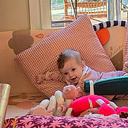 Emma participe au concours pour gagner de l'argent avec cette photo : baby, child, pink_pillow, toy, indoor, window, cushion, smiling, face, floor, play_area, soft_toys, furniture, natural_light, wood_floor, clothing, person, happy, home, relaxing