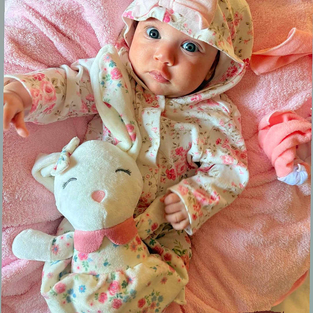 Sarah joined the competition — help win amazing prizes! baby, infant, child, hoodie, pink_blanket, stuffed_animal, toy, floral_pattern, cute, portrait, lying_down, clothing, soft_toy, young_child, baby_girl, indoors, cozy, blanket, face, expression