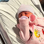 Marissa is registered to the contest to win money with this photo: newborn, baby, pacifier, pink_clothing, hat, striped_hat, m_and_ms, onesie, bed, blanket, crib, infant, sleepy, closeup, person, soft_lighting, indoors, cute, baby_toys, sleep