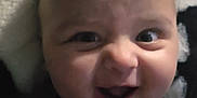 Charles is registered to the contest to win money with this photo: baby, smiling, face, child, infant, happy, clothing, tshirt, portrait, closeup, expression, lying_down, indoors, cute, person, head, skin, eyes, mouth, blanket