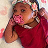 Carolina Lirisset participe au concours pour gagner de l'argent avec cette photo : baby, pacifier, red_dress, floral_headband, blanket, infant, cute, lying_down, pink, face, hand, soft_texture, pattern, closeup, indoors, child, newborn, sleepwear, portrait, relaxed