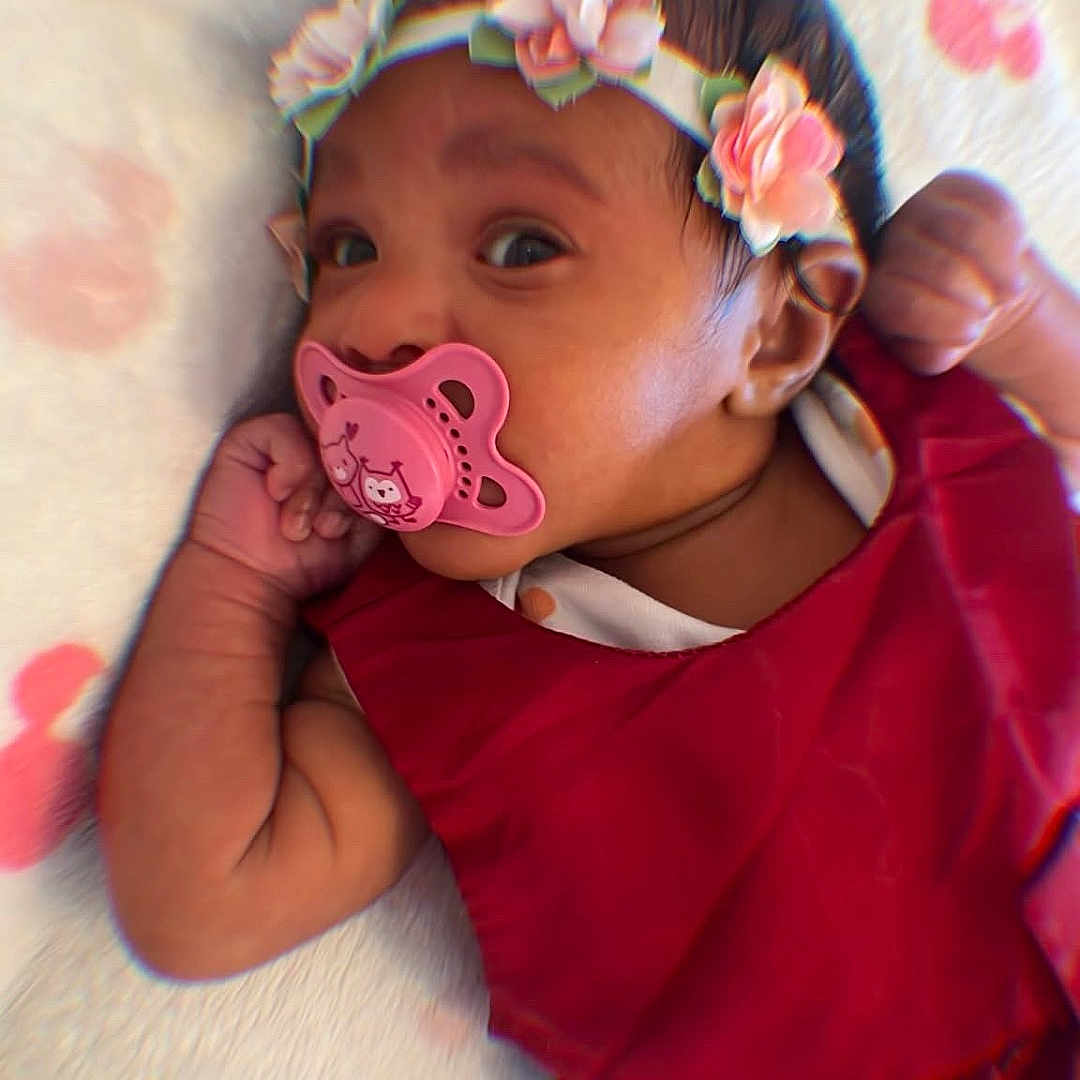 Carolina Lirisset participe au concours pour gagner de l'argent avec cette photo : baby, pacifier, red_dress, floral_headband, blanket, infant, cute, lying_down, pink, face, hand, soft_texture, pattern, closeup, indoors, child, newborn, sleepwear, portrait, relaxed