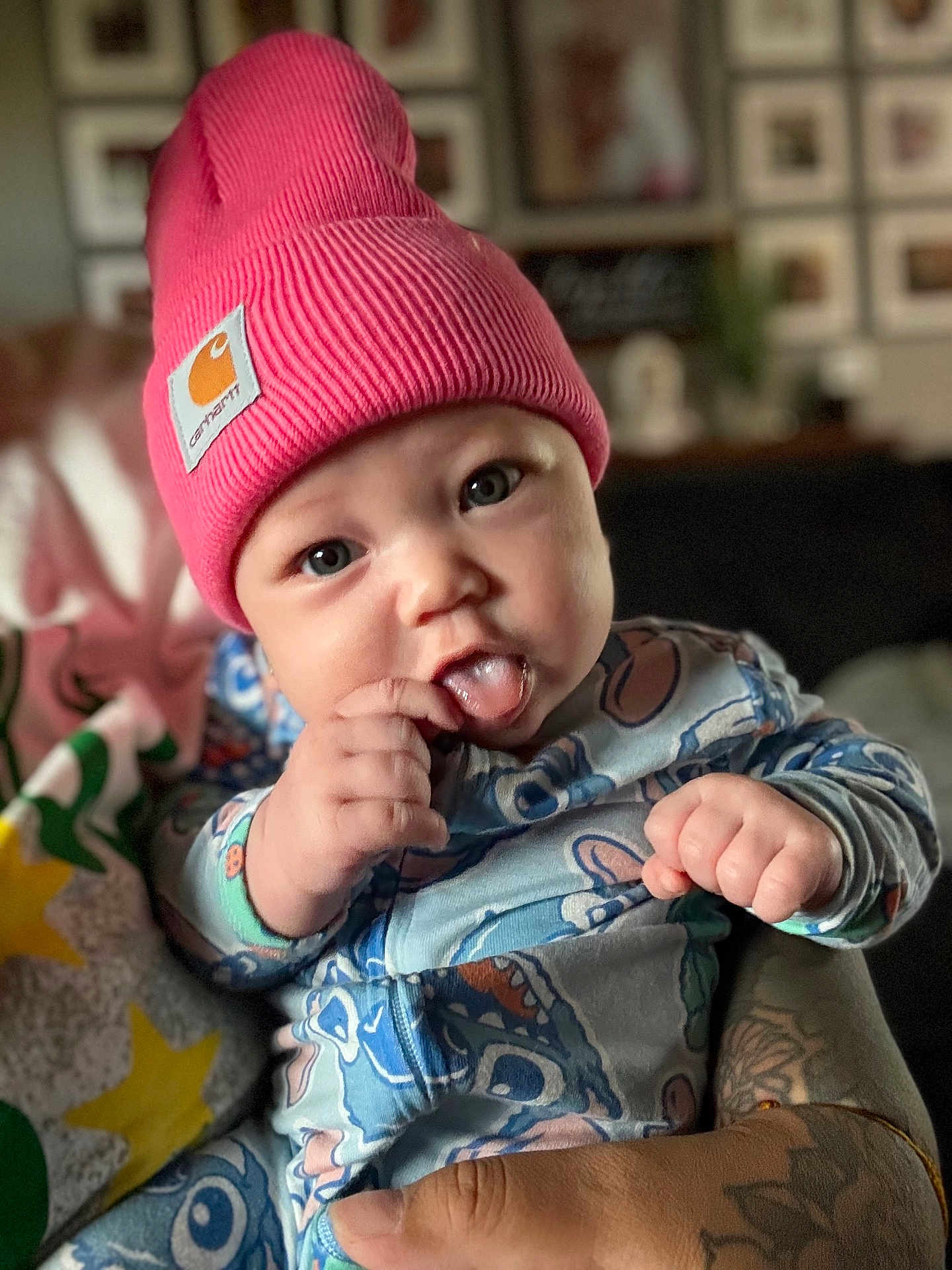 Saraiyah joined the competition — help win amazing prizes! baby, infant, child, beanie, hat, pink, onesie, patterned_clothing, tongue_out, hand, tattoo, holding, person, face, blue_eyes, indoor, home, blurred_background, cute, playful