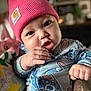 baby, infant, child, pink_beanie, onesie, hand, face, eyes, expression, curious, cute, chubby_cheeks, indoor, soft_light, blurred_background, person, portrait, clothing, sitting, toddler