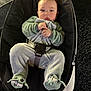 baby, baby_rocker, carpet, child, couch, cute, face, footwear, gray_clothing, green_clothing, hands, home, indoor, infant, onesie, person, portrait, seatbelt, soft_toys, yoda_slippers