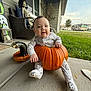 baby, pumpkin, porch, skeleton, costume, cookie_pattern, grass, house, smiling, child, outdoor, daylight, concrete, window, chair, tree, toy, holiday, fall, cute