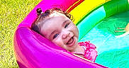Kali is registered to the contest to win money with this photo: toddler, child, pool, inflatable_pool, rainbow, grass, summer, happy, smiling, water, outdoor, play, fun, cute, baby, pink, yellow, green, blue, sunlight