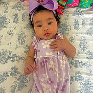 Kali joined the competition — help win amazing prizes! baby, infant, purple_outfit, headband, plush_toys, bedspread, patterned_bedspread, curly_hair, lying_down, cute, child, soft_toys, colorful, indoor, portrait, young_child, smiling, expression, hand, face