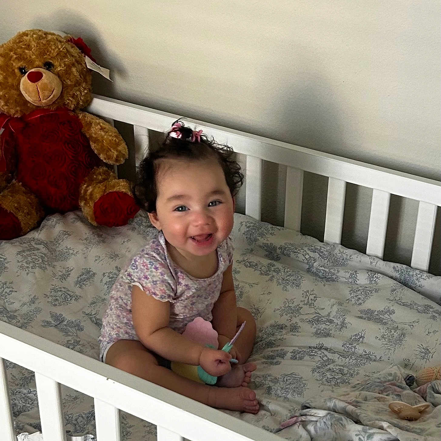 Kali joined the competition — help win amazing prizes! baby, crib, teddy_bear, toy, smiling, child, indoor, bedding, onesie, cute, happy, infant, person, nursery, furniture, plush_toy, sitting, curly_hair, portrait, home