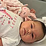 baby, infant, headband, bow, white_clothing, pink_toy, plush_toy, lying_down, closeup, face, cute, soft_texture, sleepy, child, newborn, adorable, indoors, portrait, resting, peaceful