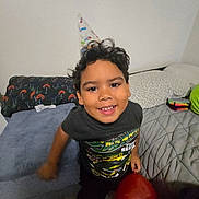 Vincent is registered to the contest to win money with this photo: balloon, bedroom, bedspread, boy, casual_clothing, celebration, child, curly_hair, cute, fun, happy, home, indoor, party_hat, person, pillow, portrait, smile, tshirt, young