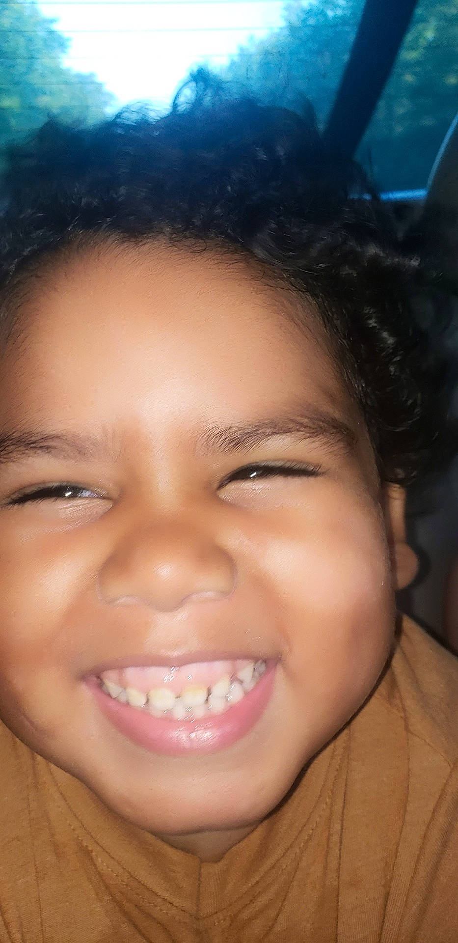 brown_shirt, child, childhood, close_up, curly_hair, cute, expression, face, fun, happy, head, indoor, joyful, natural_light, person, portrait, skin, smile, teeth, young
