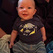 Remington is registered to the contest to win money with this photo: child, baby, infant, smiling, onesie, dinosaur_print, striped_pants, sitting, blanket, couch, portrait, face, eyes, hands, legs, fabric, cozy, cute, indoor, clothing