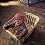 baby, laundry_basket, carpet, indoor, playpen, toys, smiling, child, home, floor, clothing, plastic, infant, sitting, cute, happy, playful, person, domestic, bright