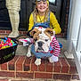 Louie joined the competition — help win amazing prizes! child, dog, bulldog, costume, halloween, candy, brick_porch, door, mummy_decoration, smiling, yellow_clothing, blue_overalls, glasses, puppy, pet, outdoor, holiday, funny_costume, toy_knife, happy