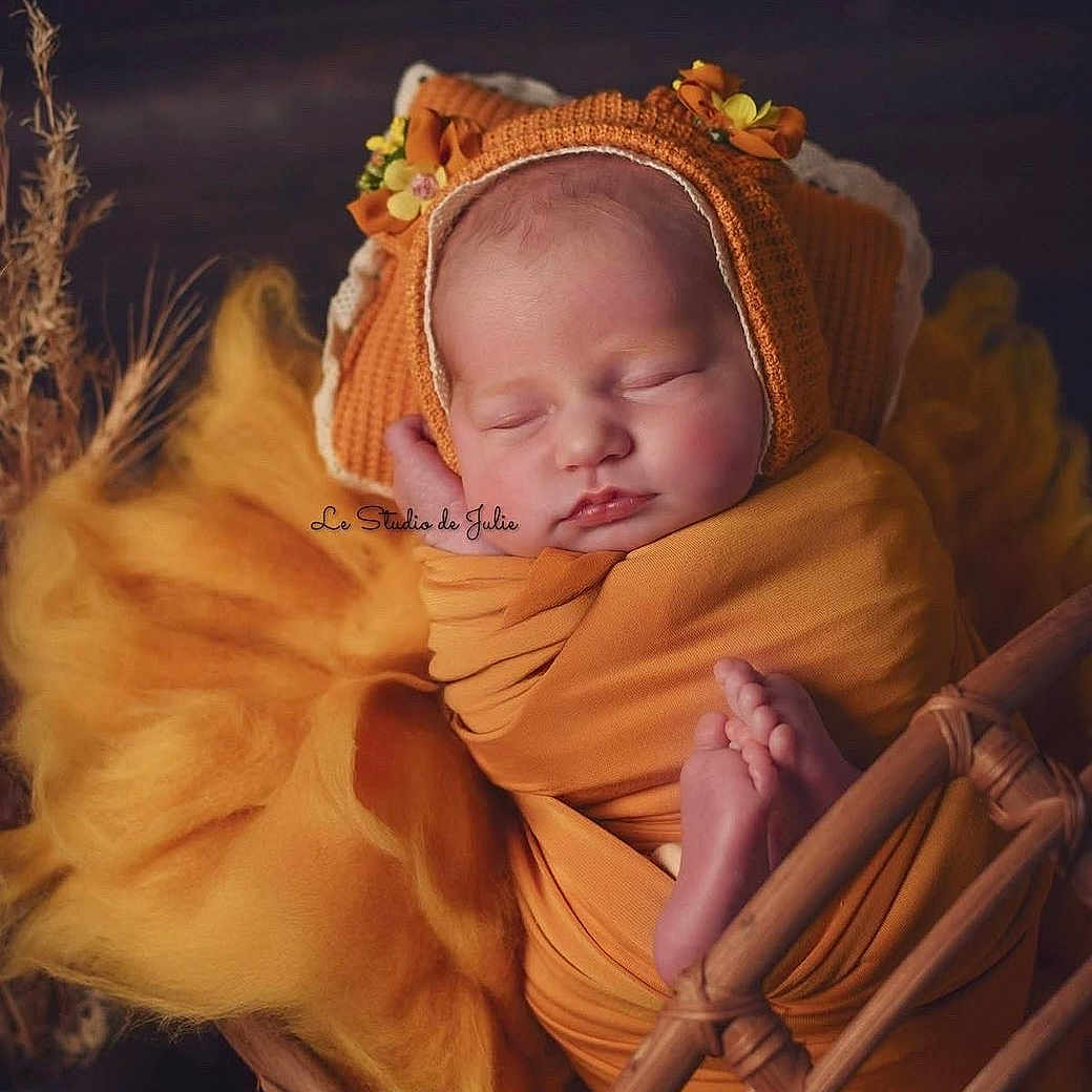 Iris participe au concours pour gagner de l'argent avec cette photo : newborn, baby, sleeping, orange, blanket, bonnet, flower, wicker_basket, yellow_fabric, cozy, autumn, portrait, infant, cute, resting, soft, peaceful, wrapped, child, indoors