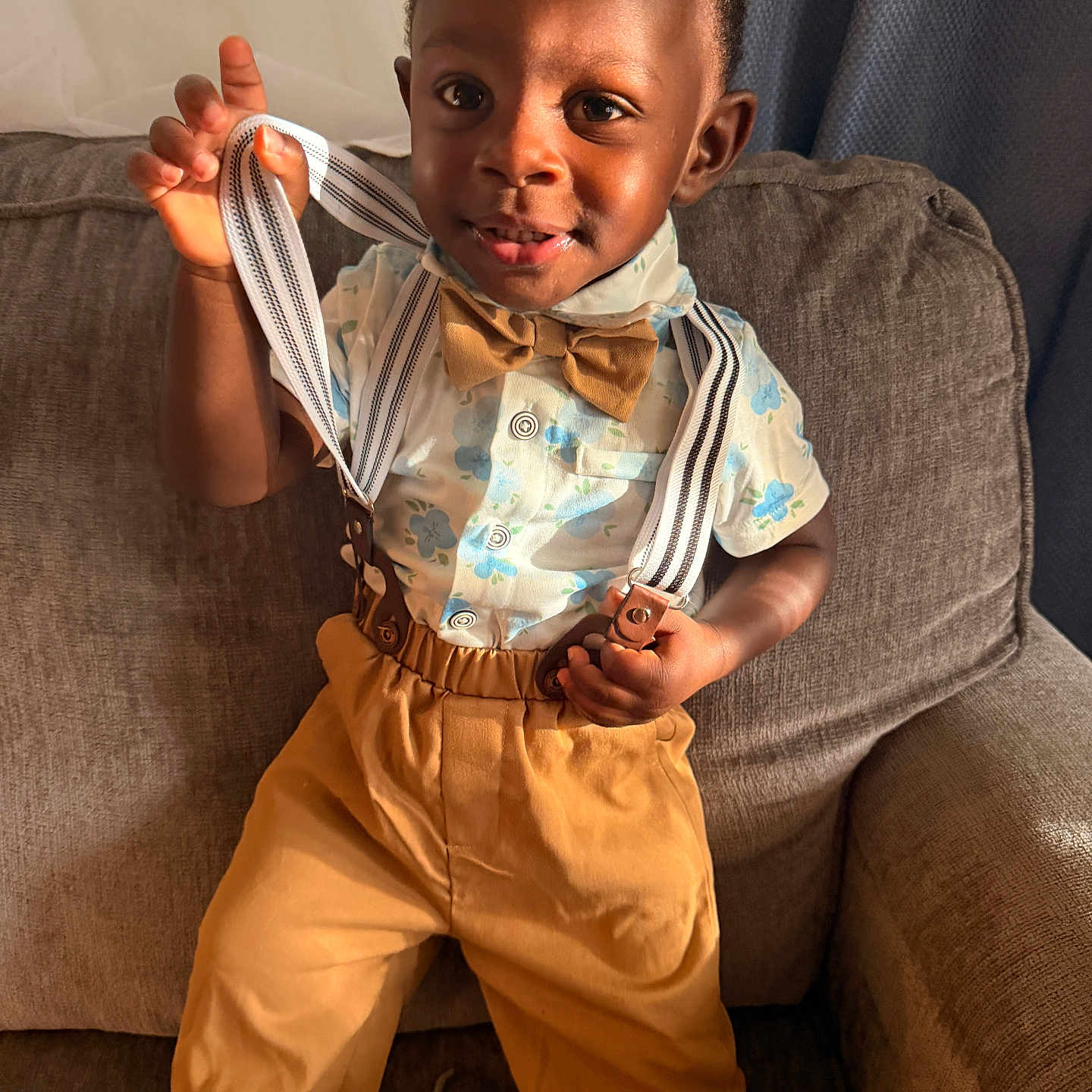 Kai is registered to the contest to win money with this photo: bow_tie, boy, casual_clothing, child, couch, curly_hair, fabric, face, hand, home, indoors, pants, playful, portrait, shirt, smile, sunlight, suspenders, toddler, window