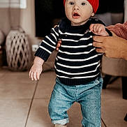 Ezio participe au concours pour gagner de l'argent avec cette photo : baby, blue_jeans, child, curtain, cute, expression, floor, furniture, hand_support, home, indoor, person, red_hat, sandals, striped_sweater, television, tile_floor, toddler, walking, young_child