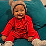Nyla-Rose joined the competition — help win amazing prizes! baby, child, smile, red_clothing, hat, knit_hat, pom_poms, sitting, couch, teal_couch, happy, indoors, portrait, cute, infant, white_socks, cozy, warm_clothing, person, face