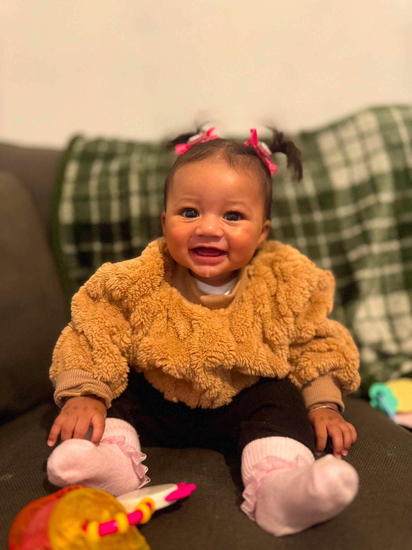 Nyla-Rose is registered to the contest to win money with this photo: baby, child, smiling, pigtails, pink_bows, brown_sweater, pink_socks, toy, couch, plaid_blanket, happy, indoor, portrait, infant, cute, sitting, cozy, face, hands, feet